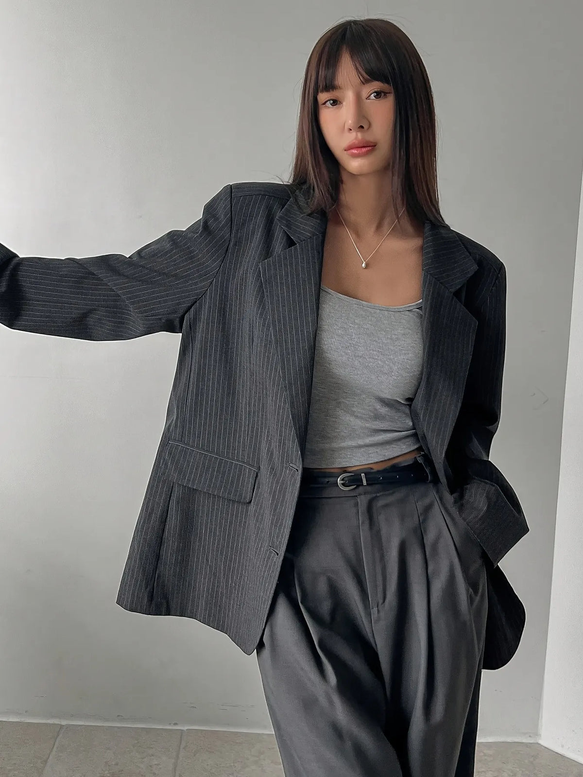 Person wearing a black blazer over a gray top and pants in a minimalistic setting
