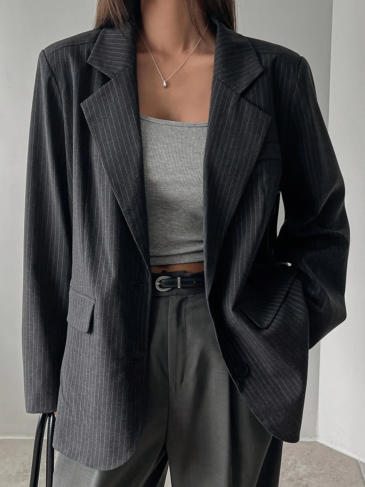 Person wearing a dark pinstripe blazer over a gray top and pants on a neutral background