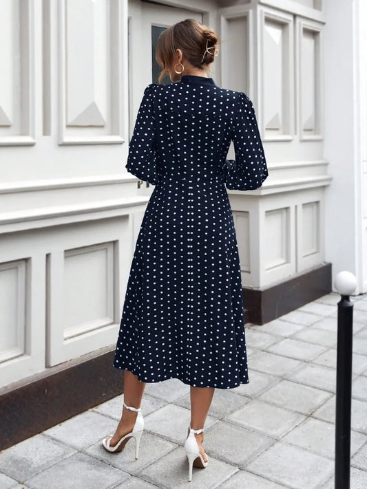 Woman wearing a navy blue dress with white polka dots in an urban setting.