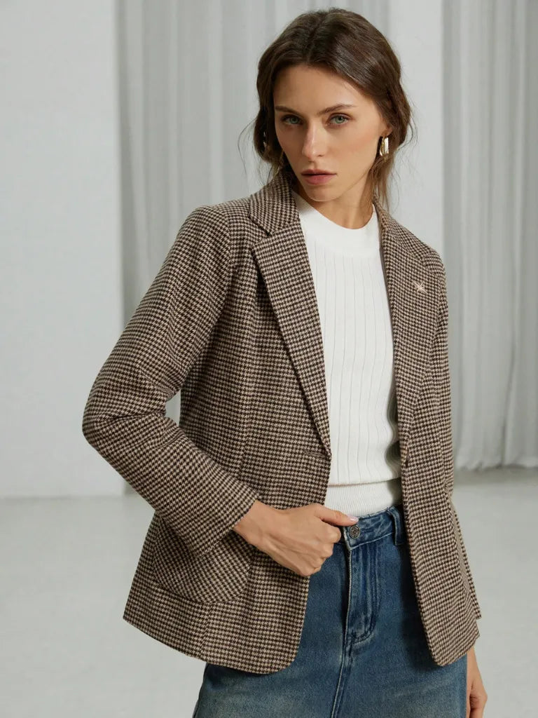 Woman wearing a brown checkered blazer over a white sweater and blue jeans on a light background