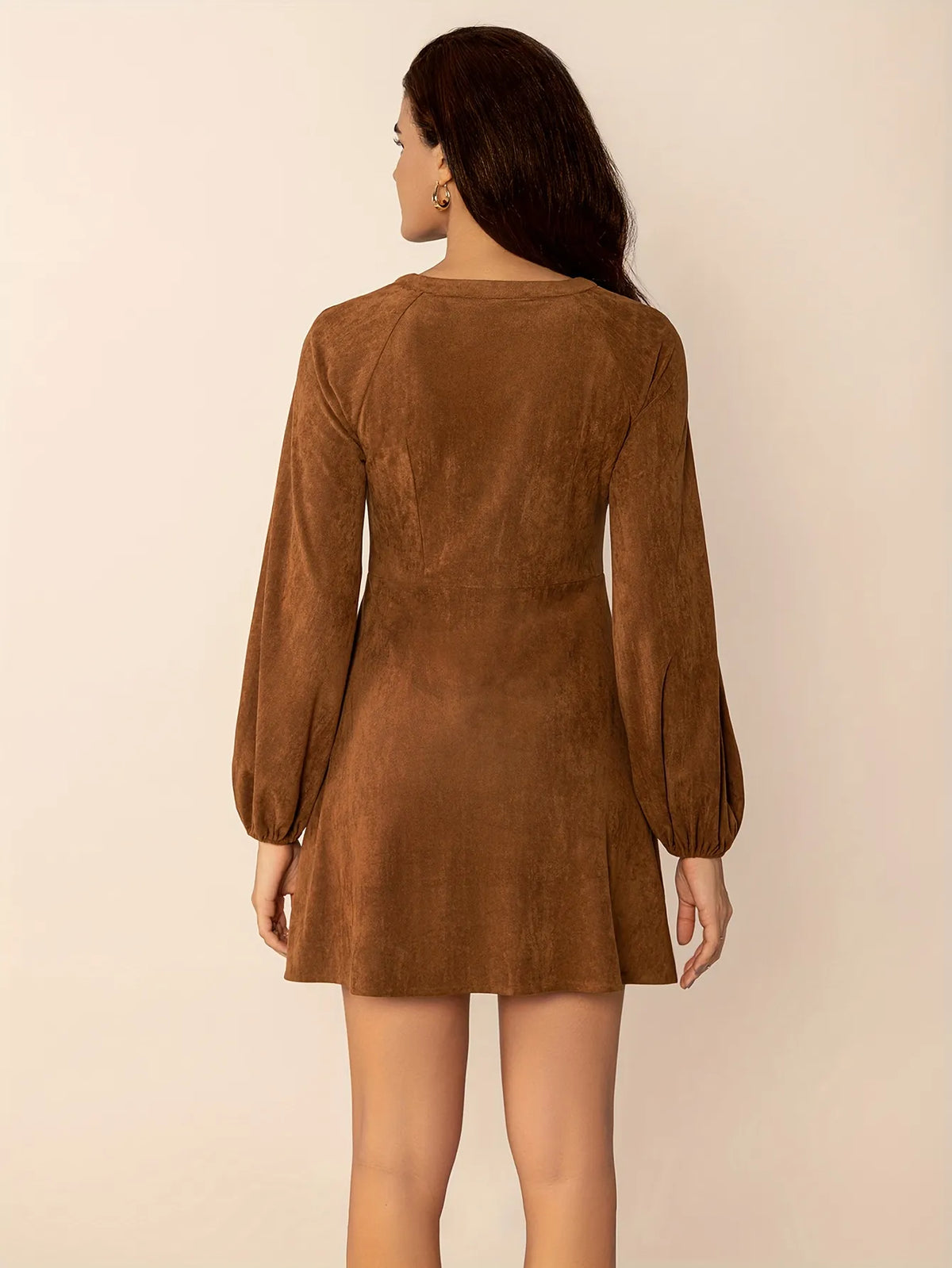 
Woman wearing a short brown button-up dress with long puffed sleeves and embroidered lace detail on the chest. The dress has a relaxed fit and a soft suede-like texture, styled with simple gold hoop earrings.