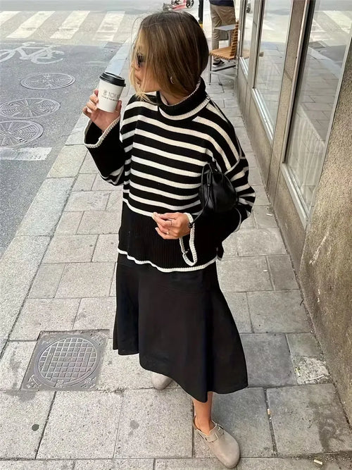 Woman in a black and white striped sweater and black skirt holding a coffee cup on a sidewalk.