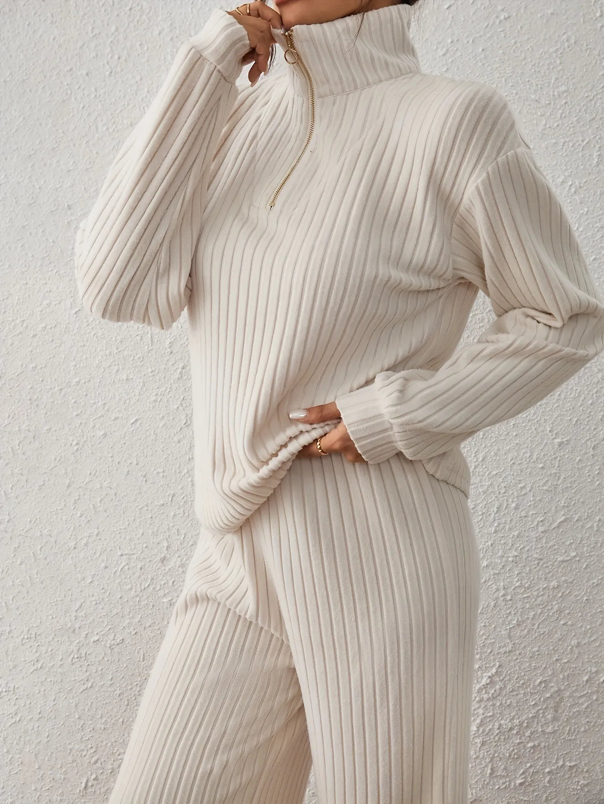 Person wearing a cream ribbed knit sweater and pants against a light gray background