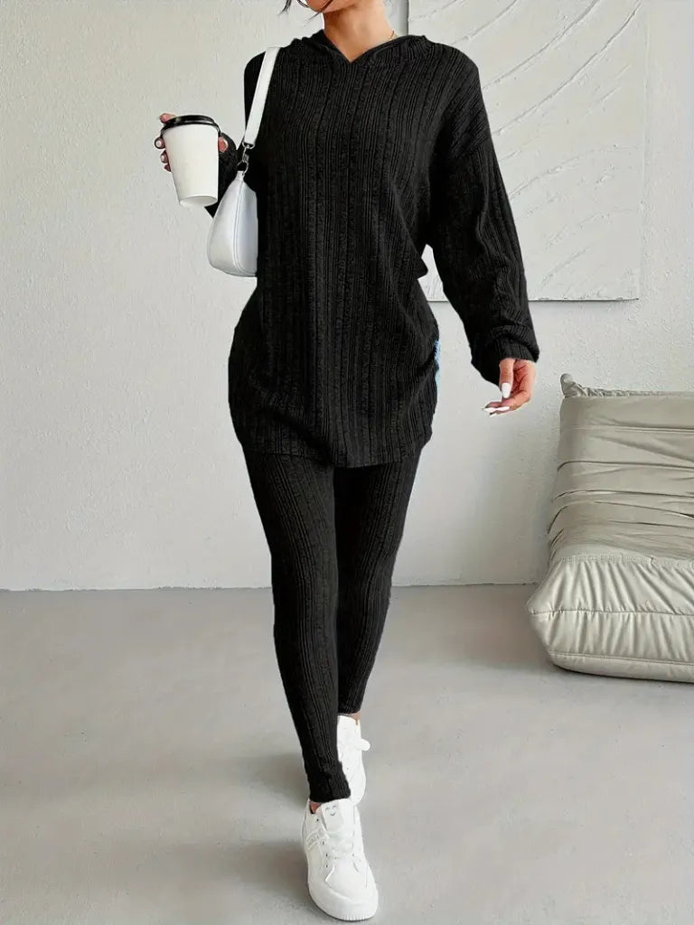 Person wearing a black outfit with white sneakers in a minimalistic room.