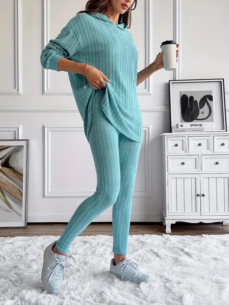 Person wearing a teal knit outfit holding a coffee cup in a room with white walls and furniture.