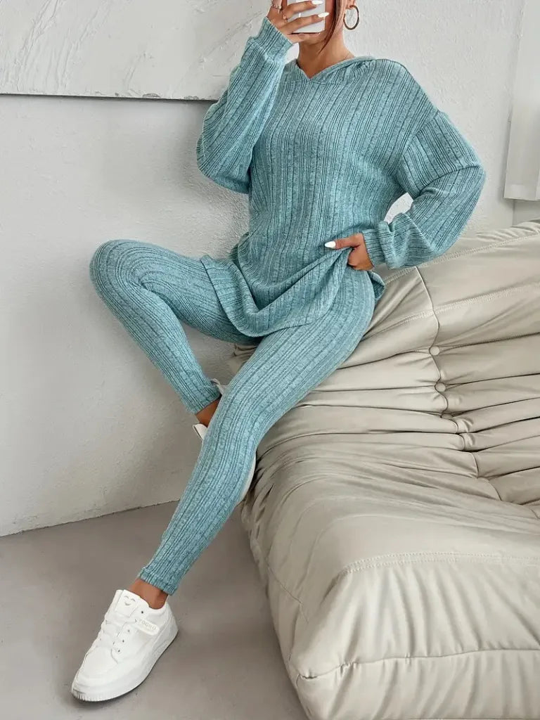 Person wearing a teal ribbed sweater and leggings set sitting on a beige sofa.