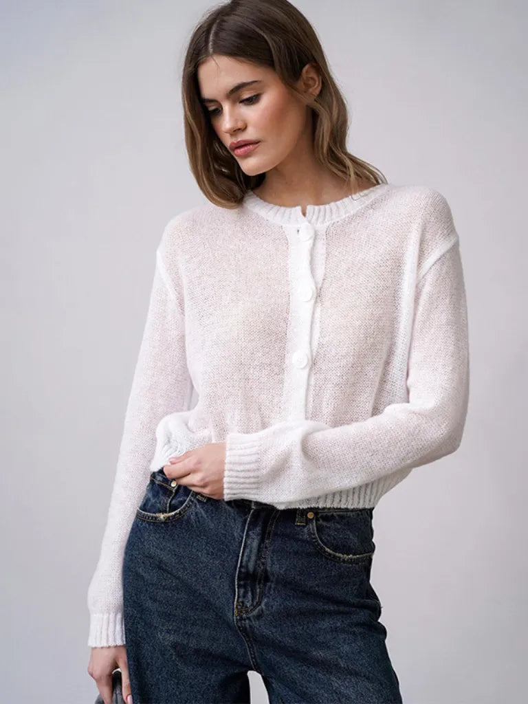 Woman wearing a white sweater and blue jeans against a plain background
