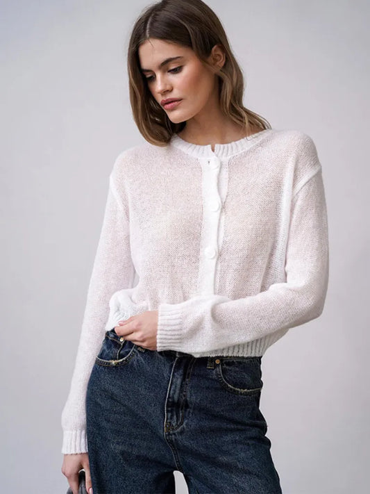 Woman wearing a white sweater and blue jeans against a plain background
