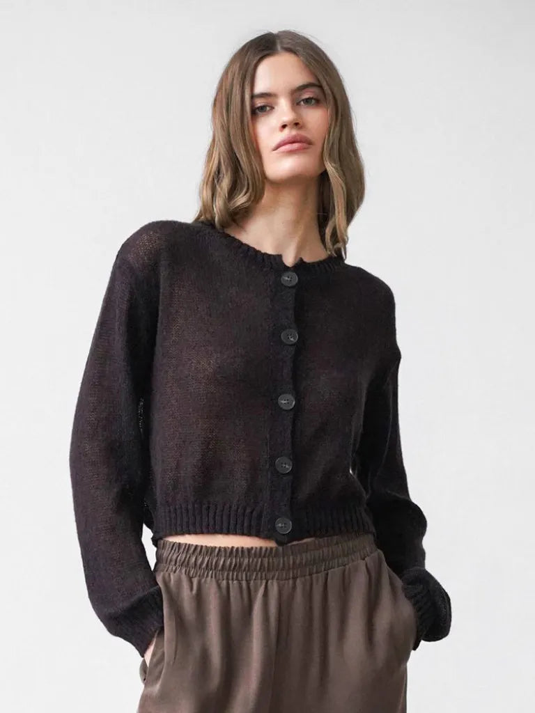 Woman wearing a dark brown cardigan and light brown pants against a white background