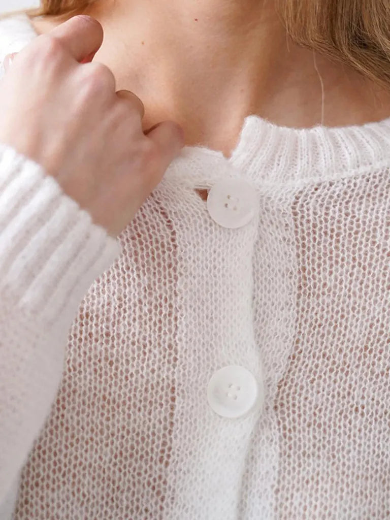 Close-up of a person wearing a white knit cardigan with buttons.