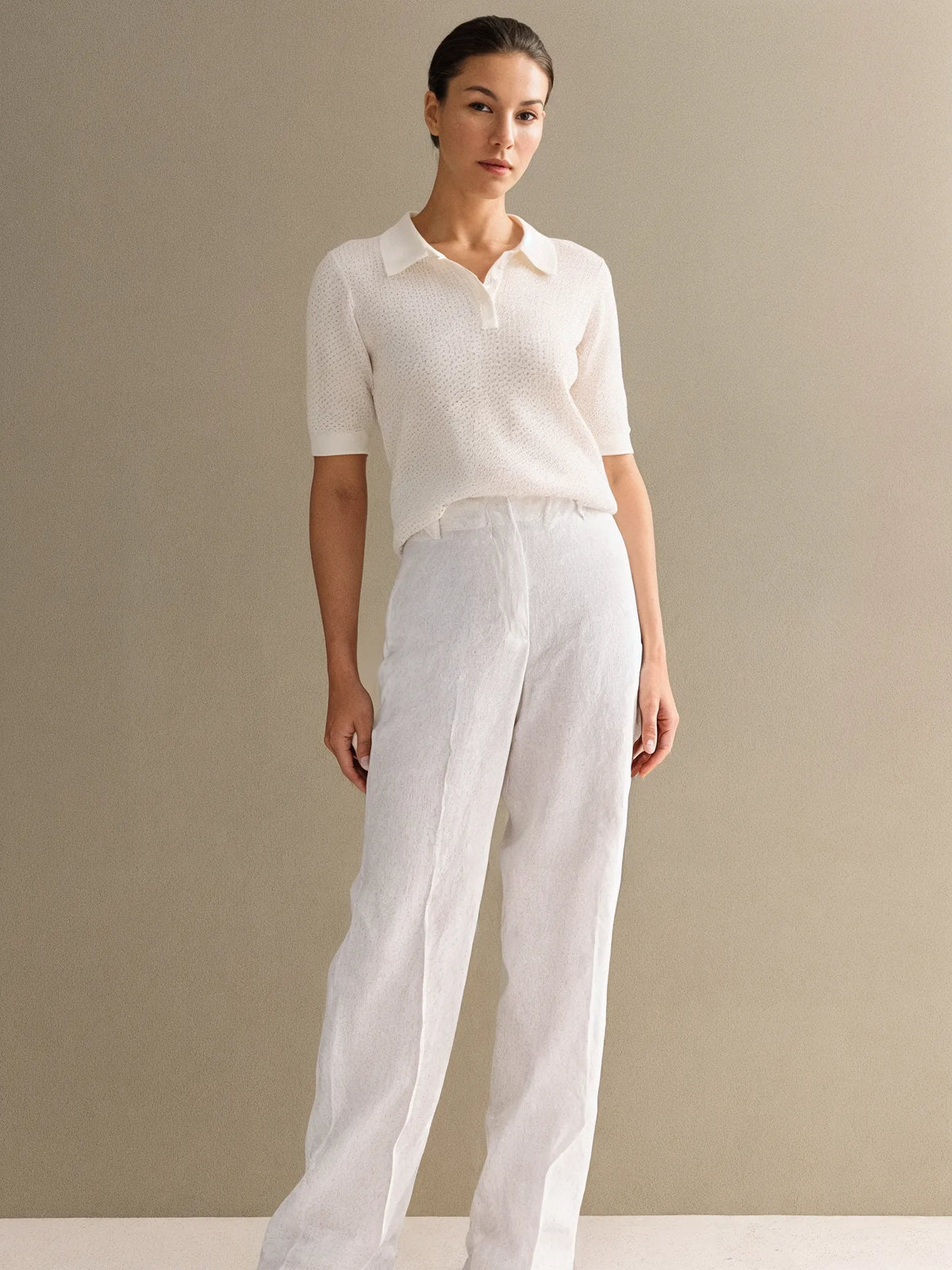 Woman wearing a white knit top and white pants against a beige background