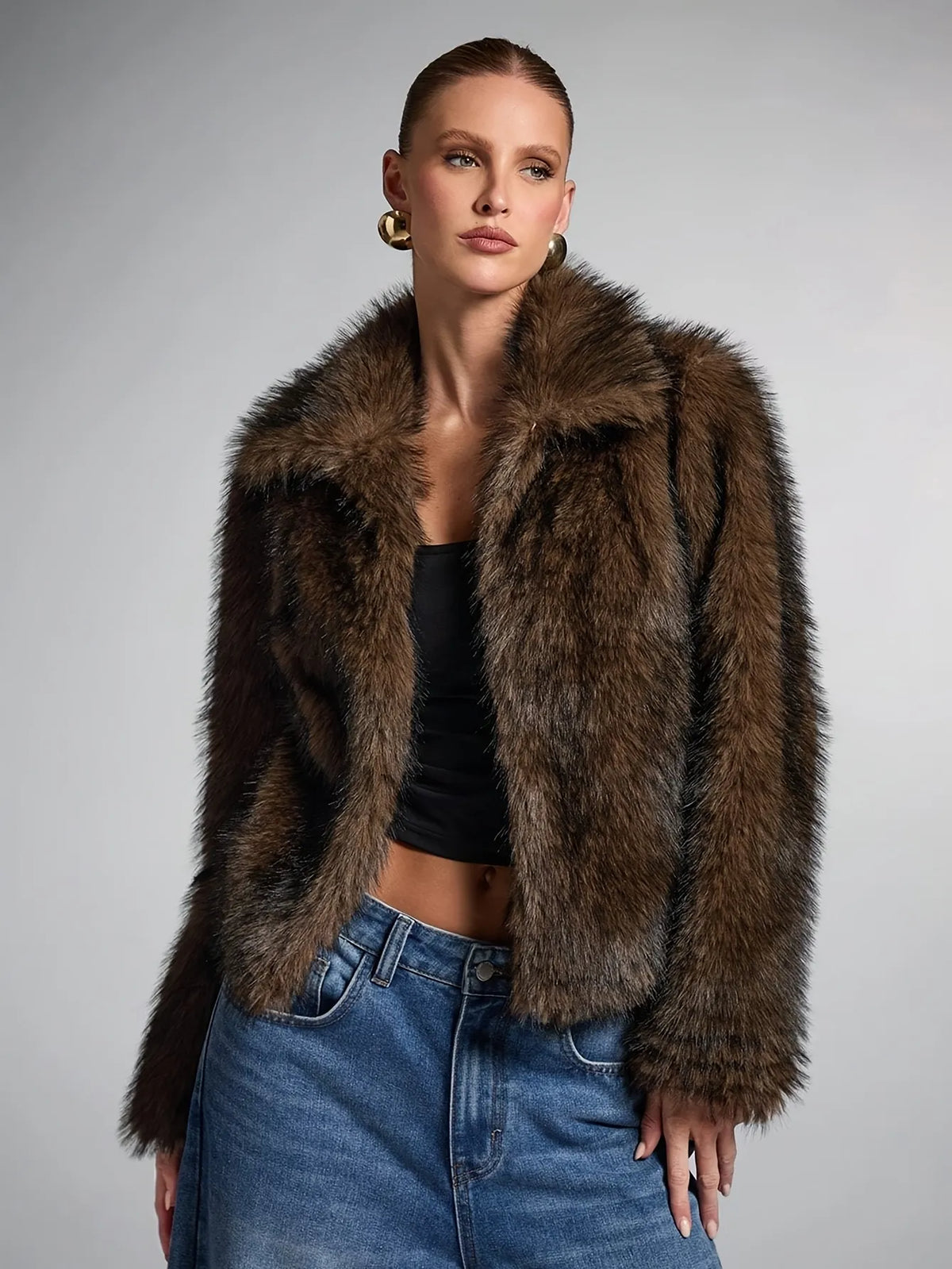 Woman wearing a brown fur jacket and blue jeans against a gray background