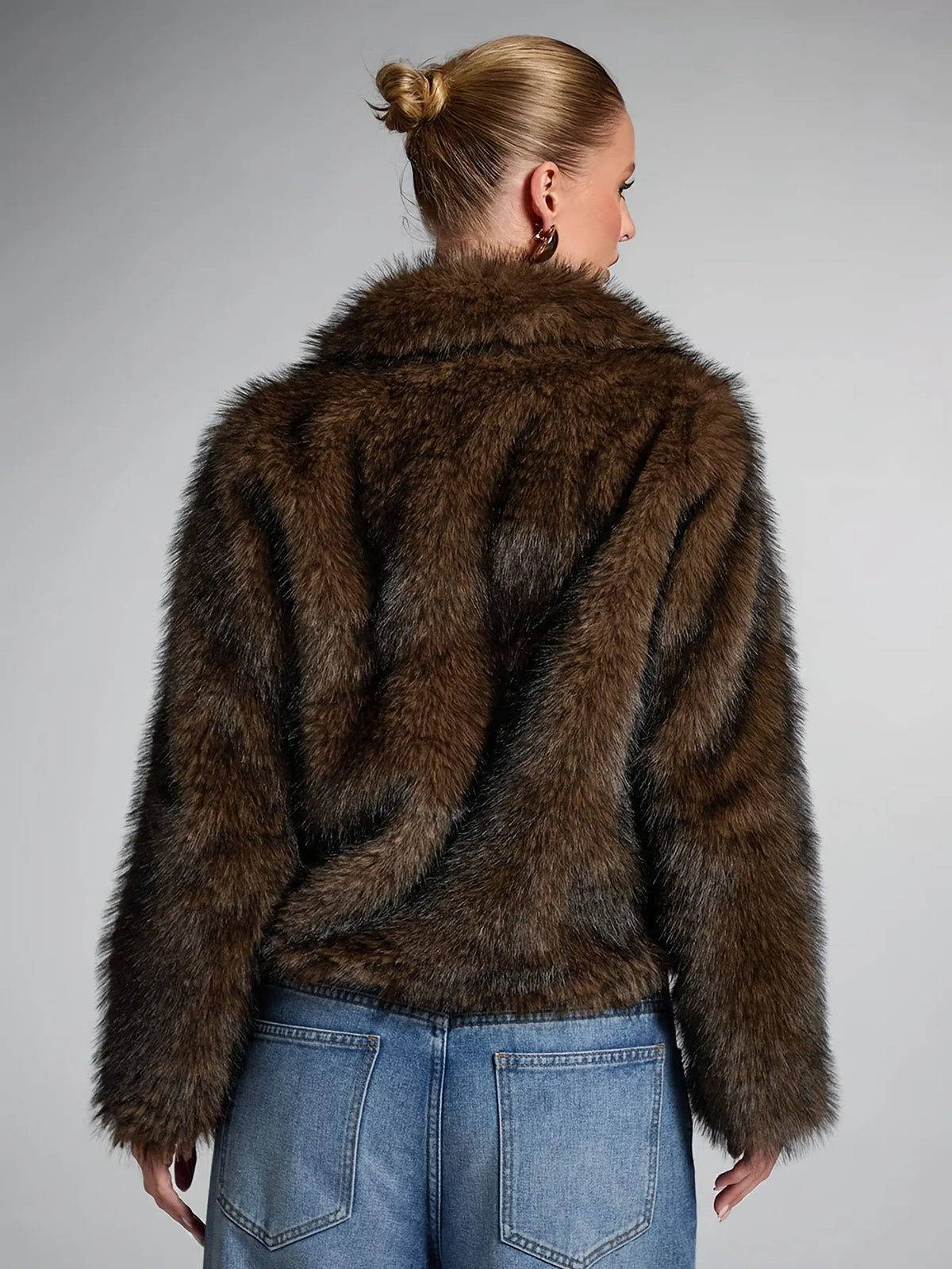 Person wearing a brown fur coat and blue jeans on a gray background