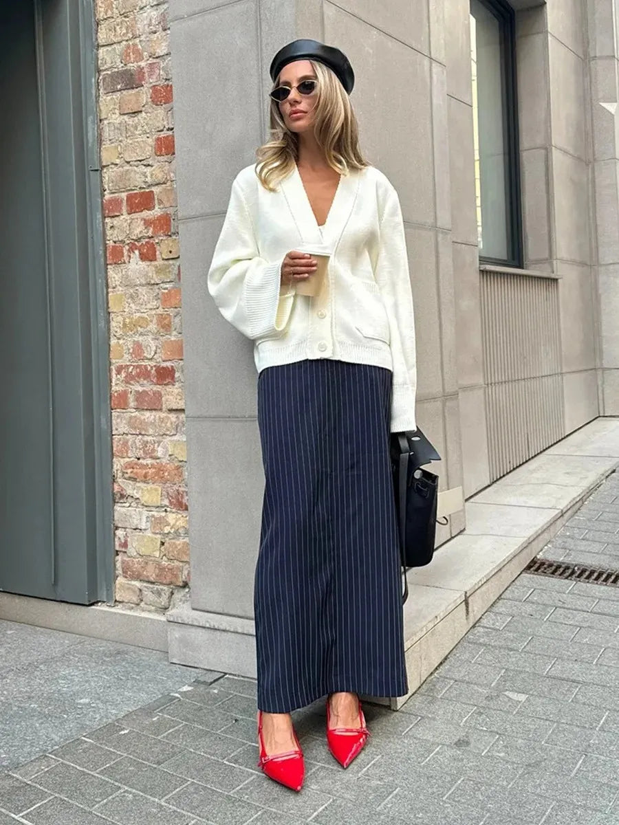 Woman in a white sweater and navy pinstripe skirt standing on a city street.