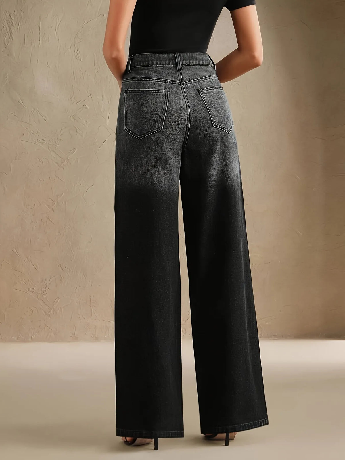 Person wearing black wide-leg jeans against a beige background