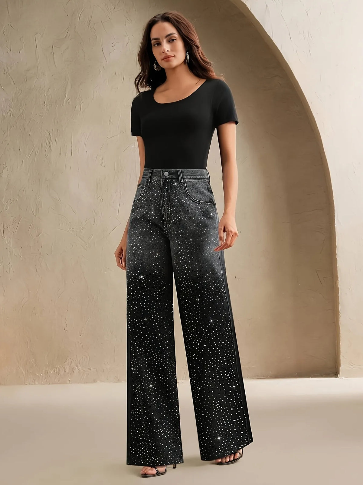 Woman wearing black studded jeans and a black top against a beige wall.