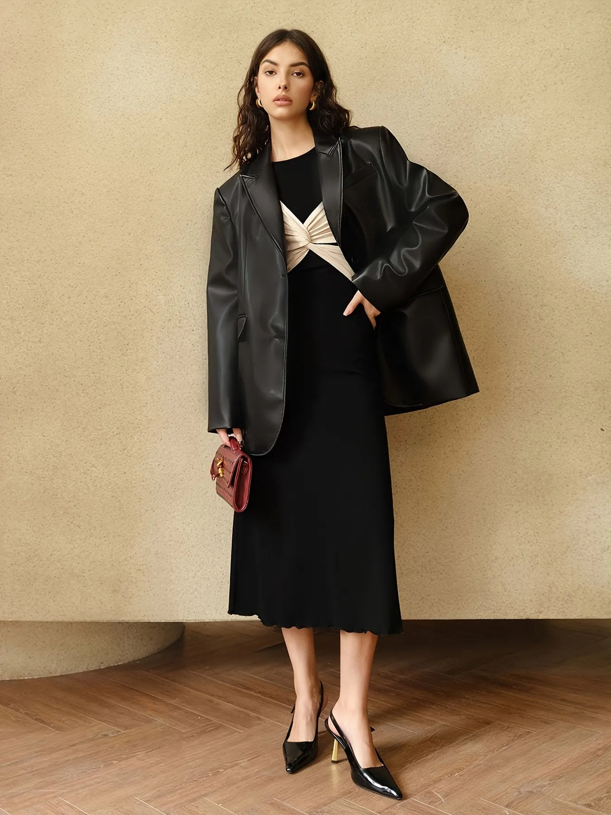 Woman wearing a long black dress with beige twist-front detail and flared sleeves. The dress has a fitted silhouette with a contrasting bodice design, styled with subtle gold hoop earrings and loose wavy hair.