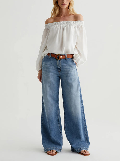Woman wearing a white off-shoulder top and blue jeans on a white background