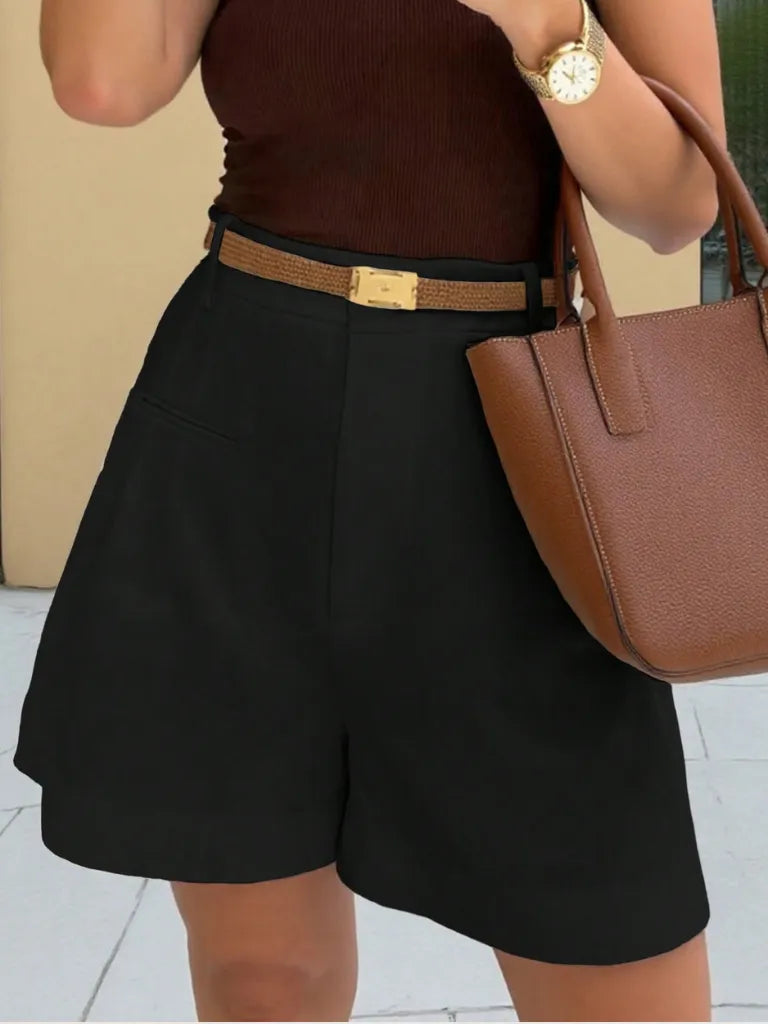 Person wearing a brown top and black shorts with a brown belt, holding a brown handbag.