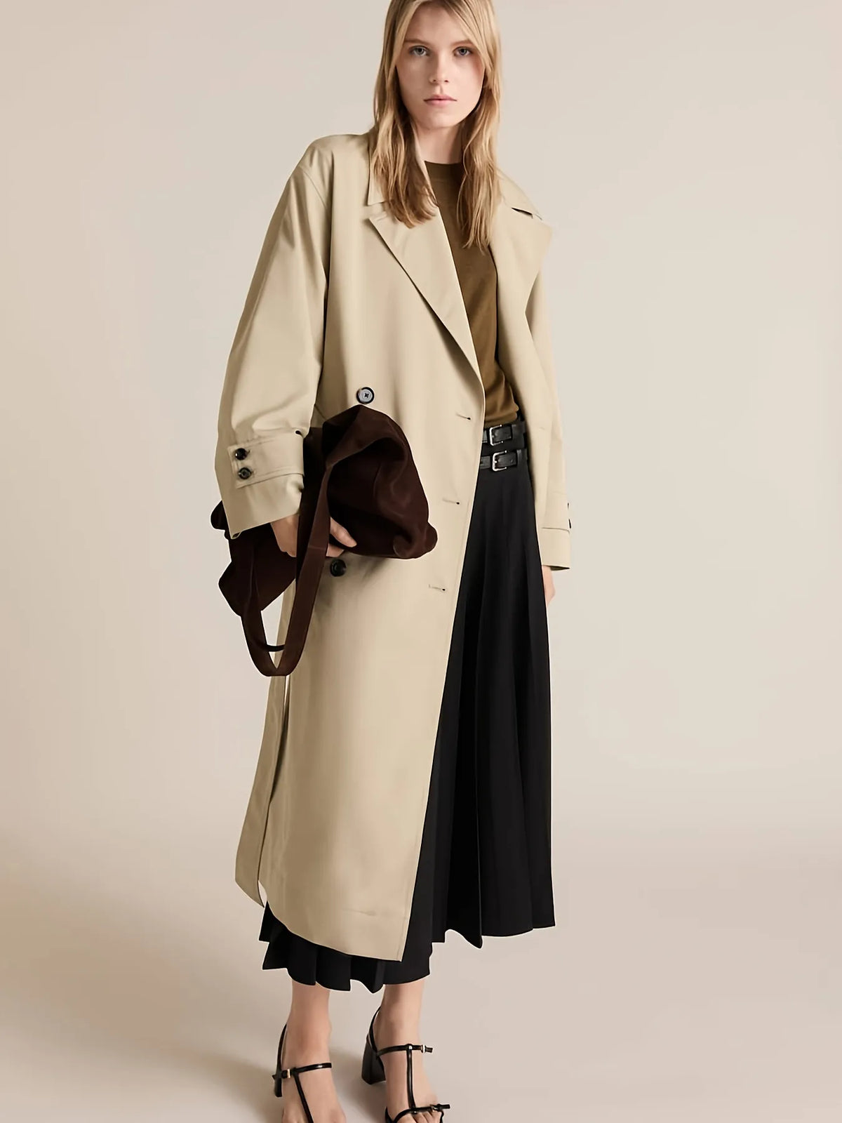 Woman wearing a beige trench coat with a black skirt and brown jacket on a plain background