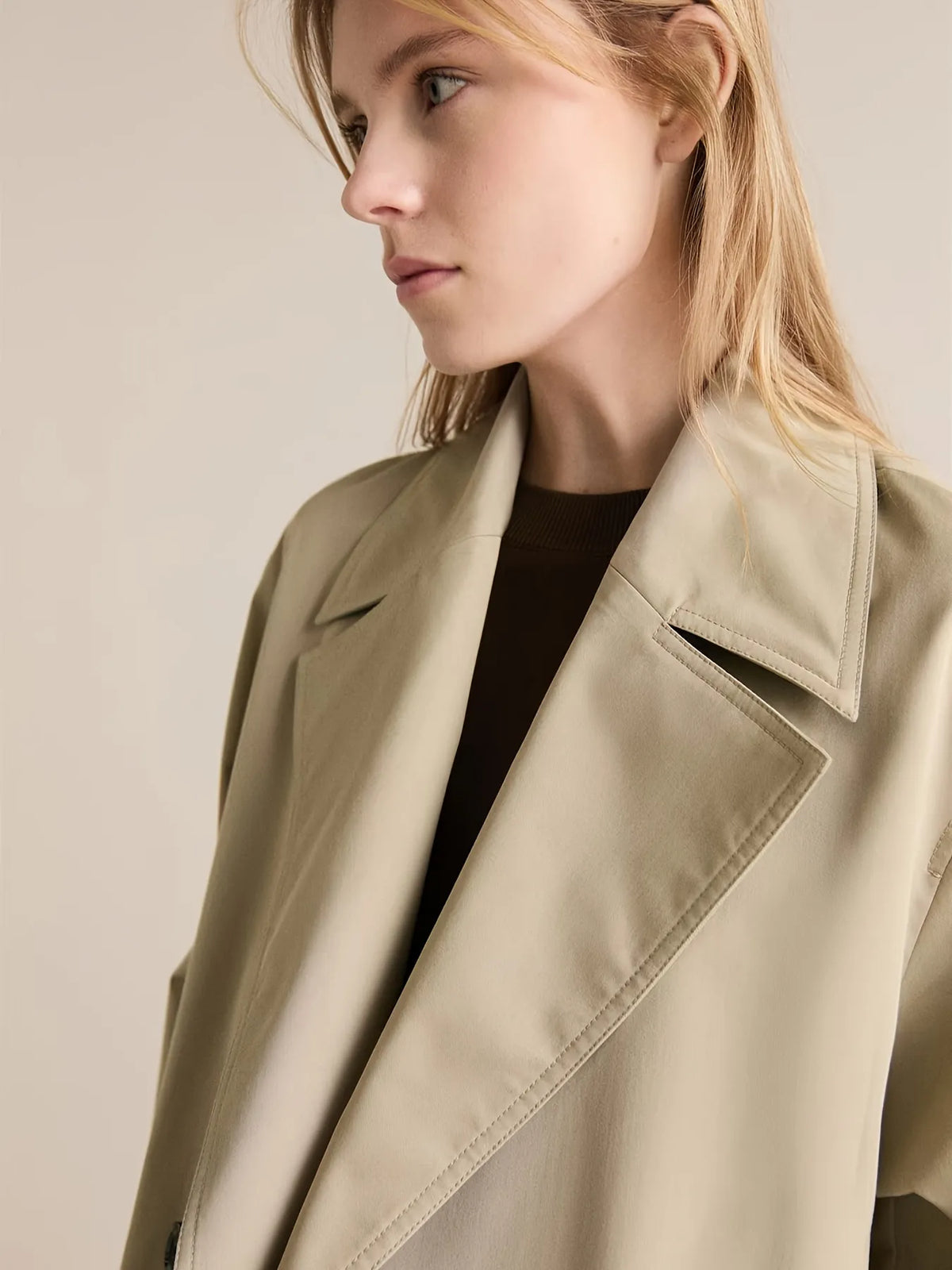 Woman wearing a beige trench coat against a neutral background