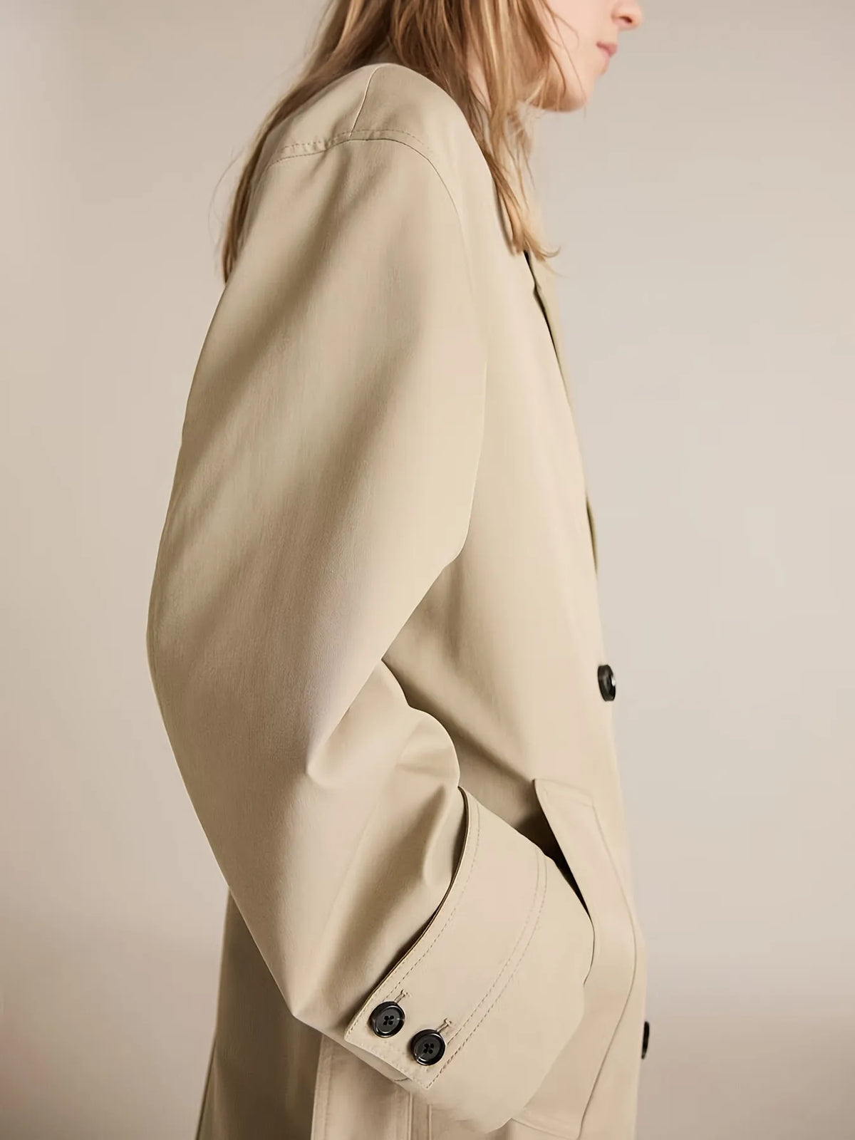 Beige trench coat worn by a person on a plain background