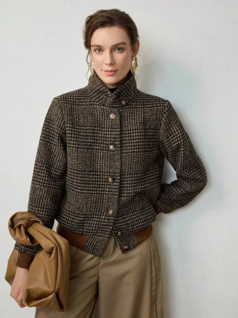 Woman wearing a plaid jacket holding a coat against a plain background