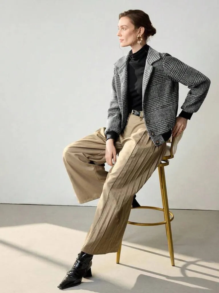 Person sitting on a stool wearing a checkered jacket, black shirt, beige pants, and black boots.
