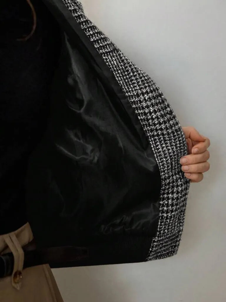 Close-up of a black coat with houndstooth patterned trim on a white background