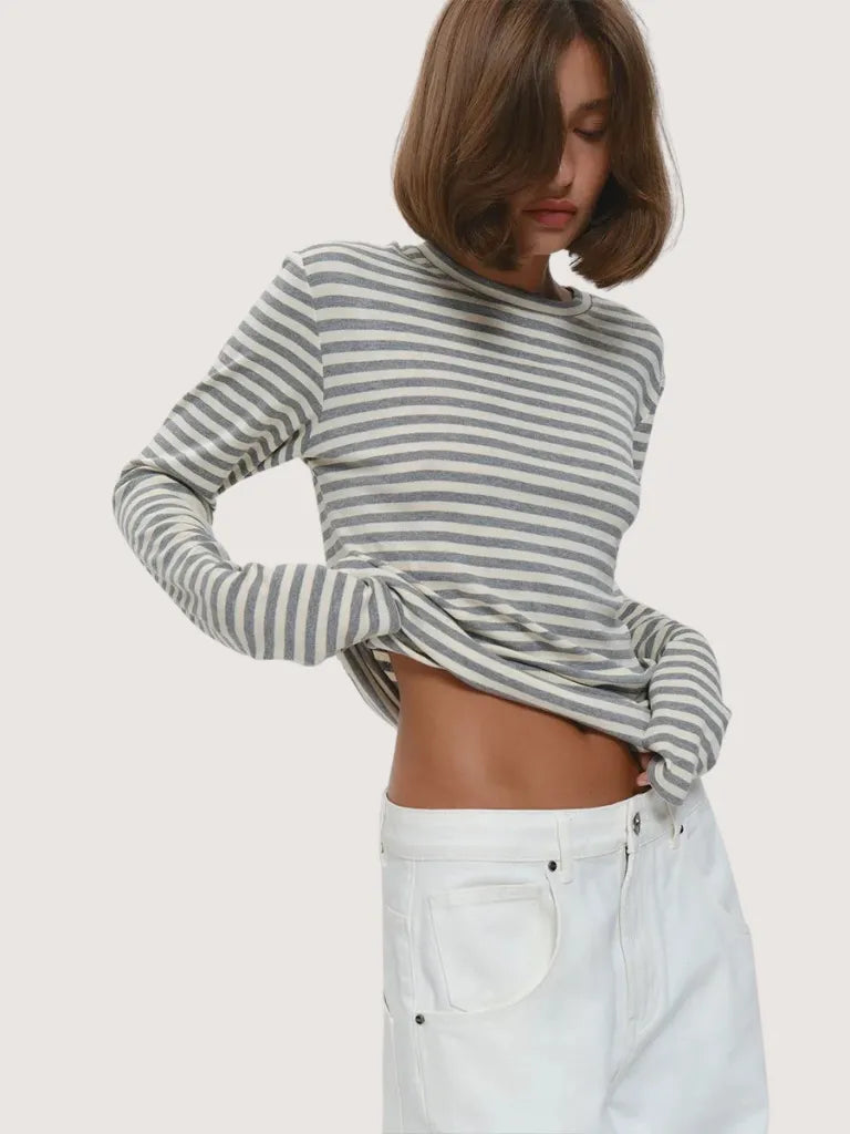 Person wearing a gray and white striped long-sleeve top with white pants on a plain background