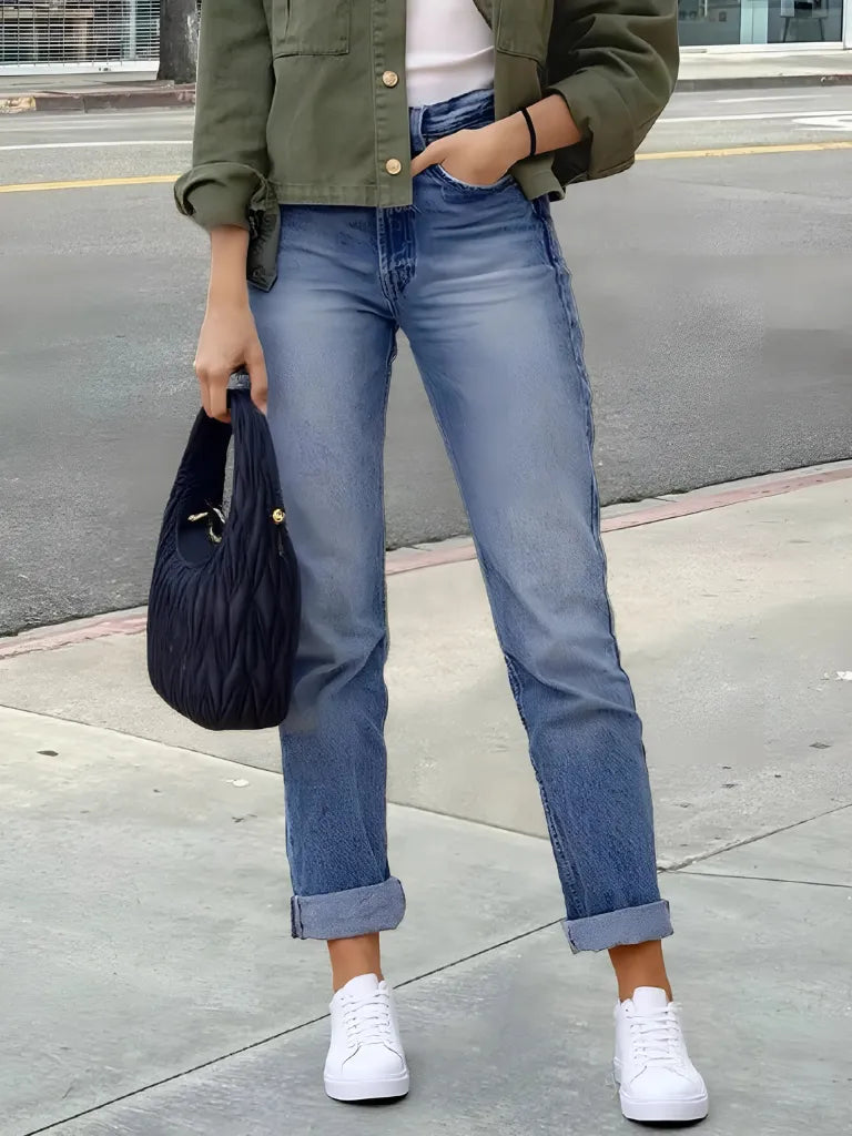 Person wearing blue jeans, a green jacket, and white sneakers on a city street.
