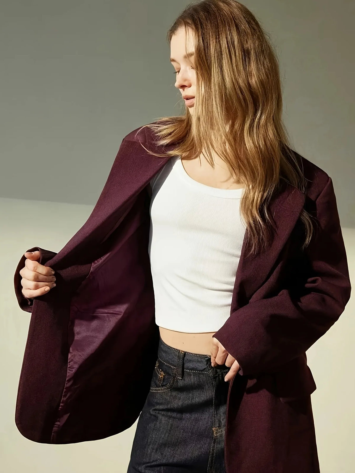 Woman wearing a burgundy blazer over a white top and dark pants on a neutral background