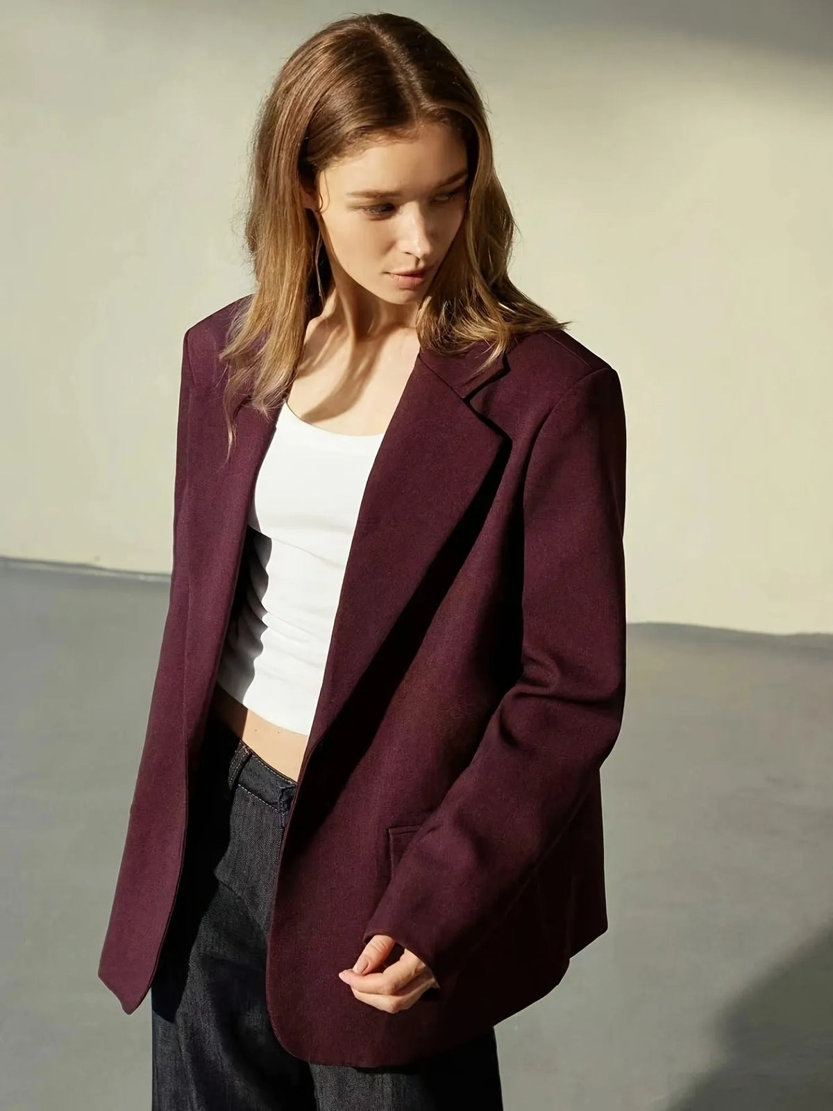 Woman wearing a burgundy blazer over a white top and dark pants on a neutral background