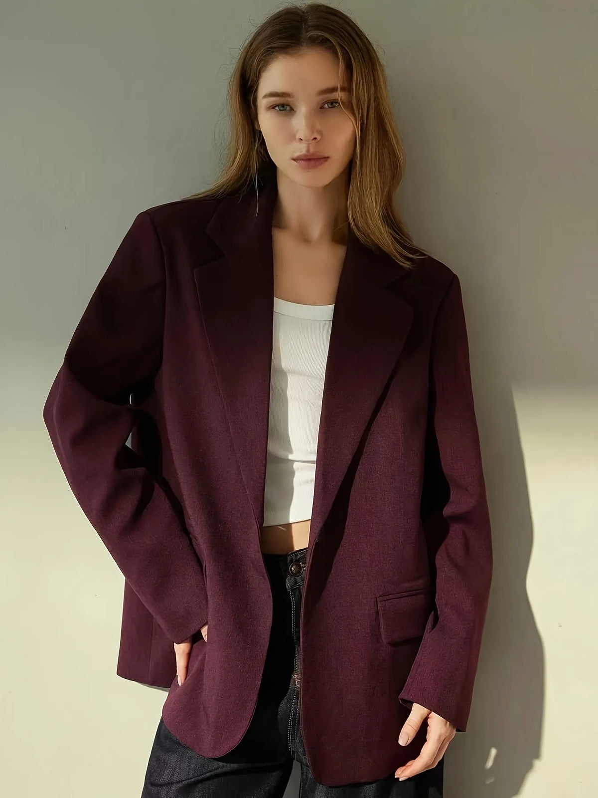 Woman wearing a burgundy blazer over a white top and dark pants on a neutral background